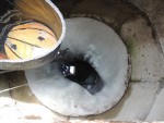 You are looking down a well in Mongolia.On the left is a bucket with clear water in it. In the middle of the well is clear water surrounded by about a foot thick ice sides. Concrete wall. All is only about a foot below the earth surface. ..in June.